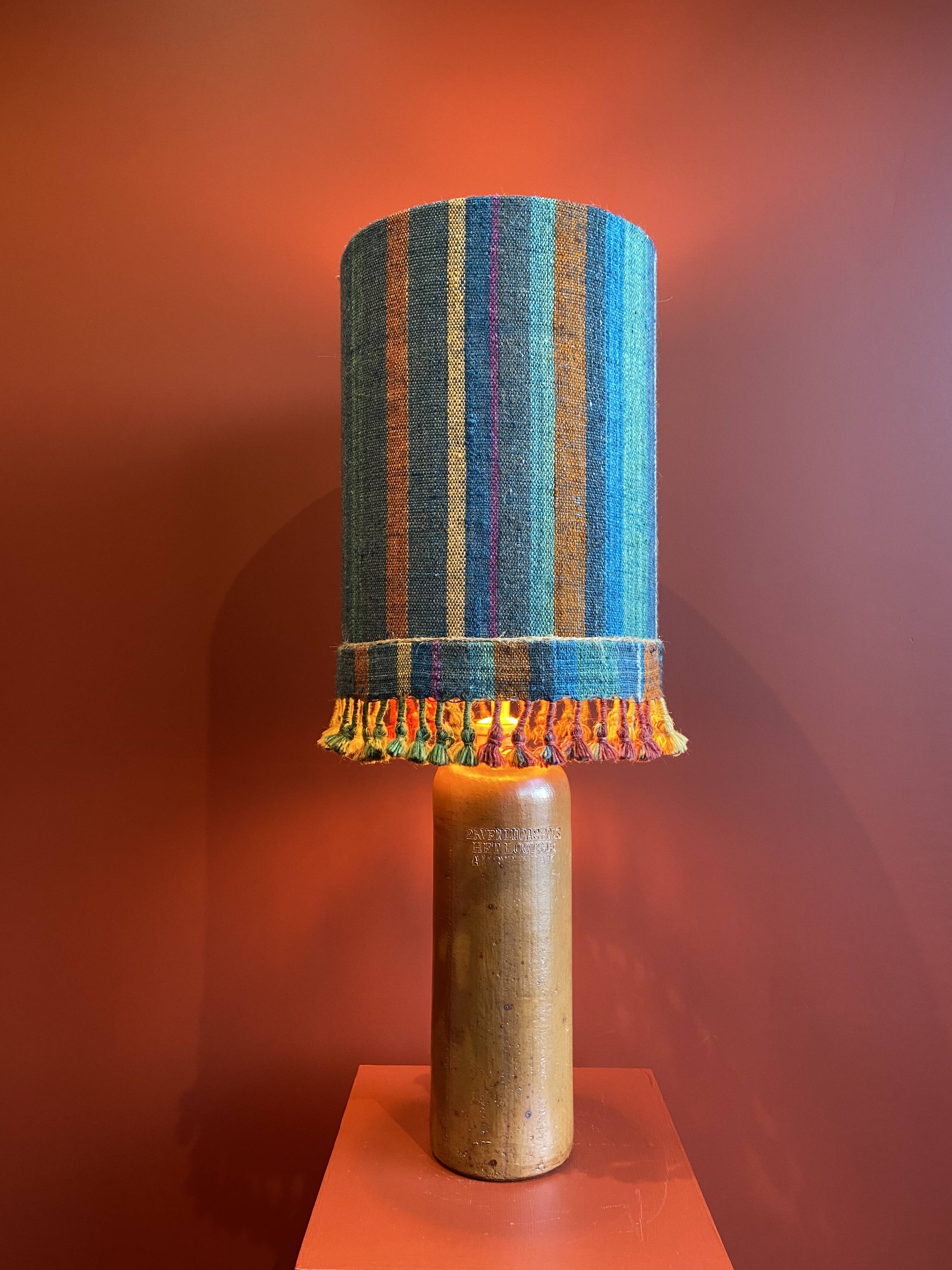 "Stoneware Bottle Lamp" with a multicoloured blue lampshade handwoven in India.
