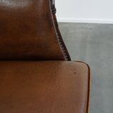 Subtle, neat sheepskin leather club armchair with a fixed seat cushion in a deep, dark cognac color