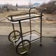 Two-tier bar cart in gold-plated brass with transparent glass shelves, yellow finish.