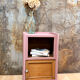 Pink bedside table with haberdashery and raw wood.