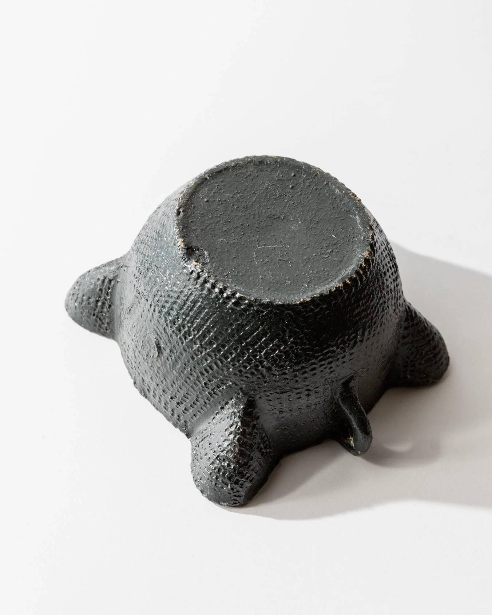 Vintage ceramic ashtray from the 1960s, black, hand-sculpted texture, organic shape.