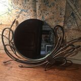 Round mirror surrounded by art deco style metal plants