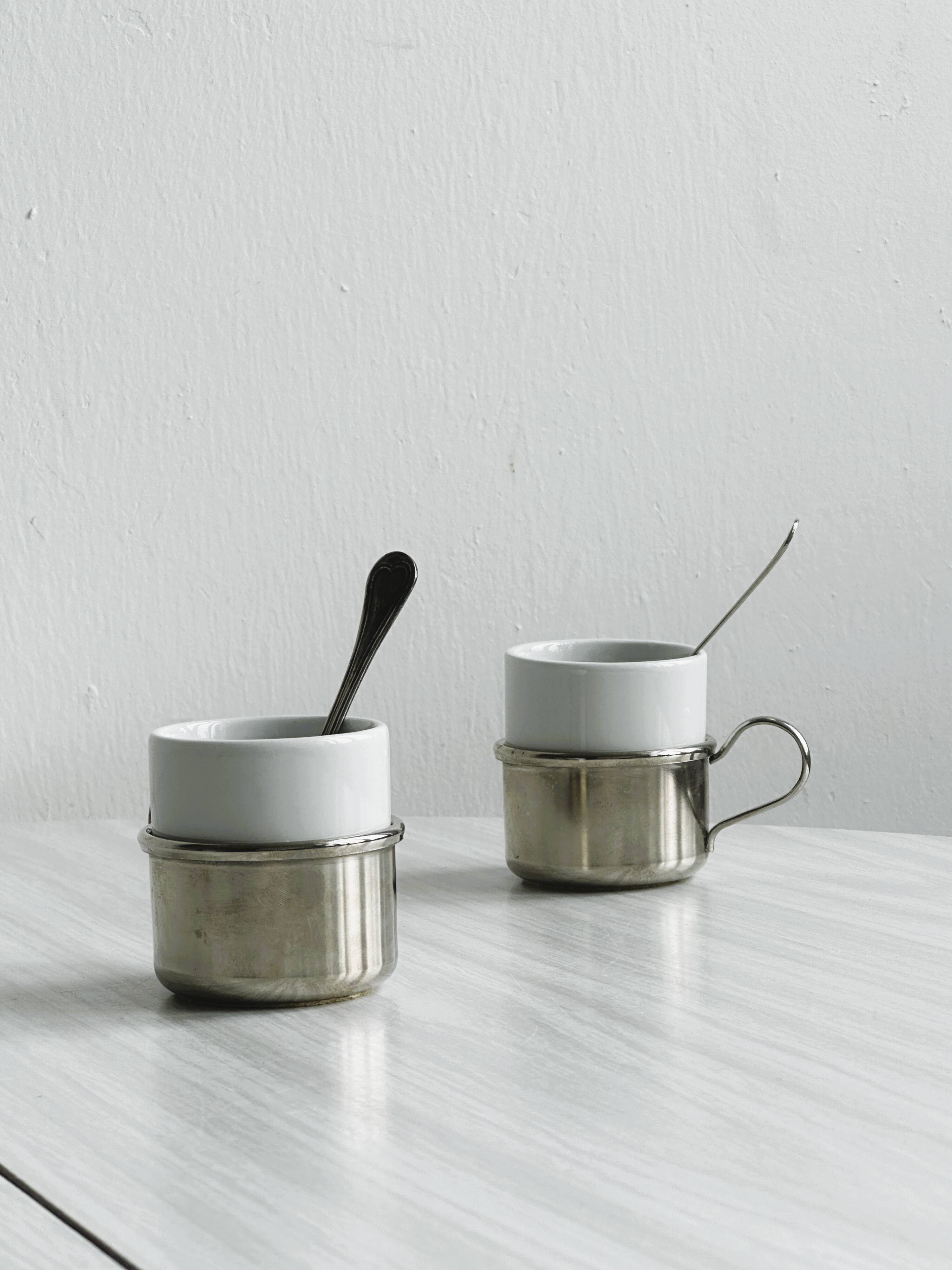 2 porcelain cups with metal supports and small spoons.