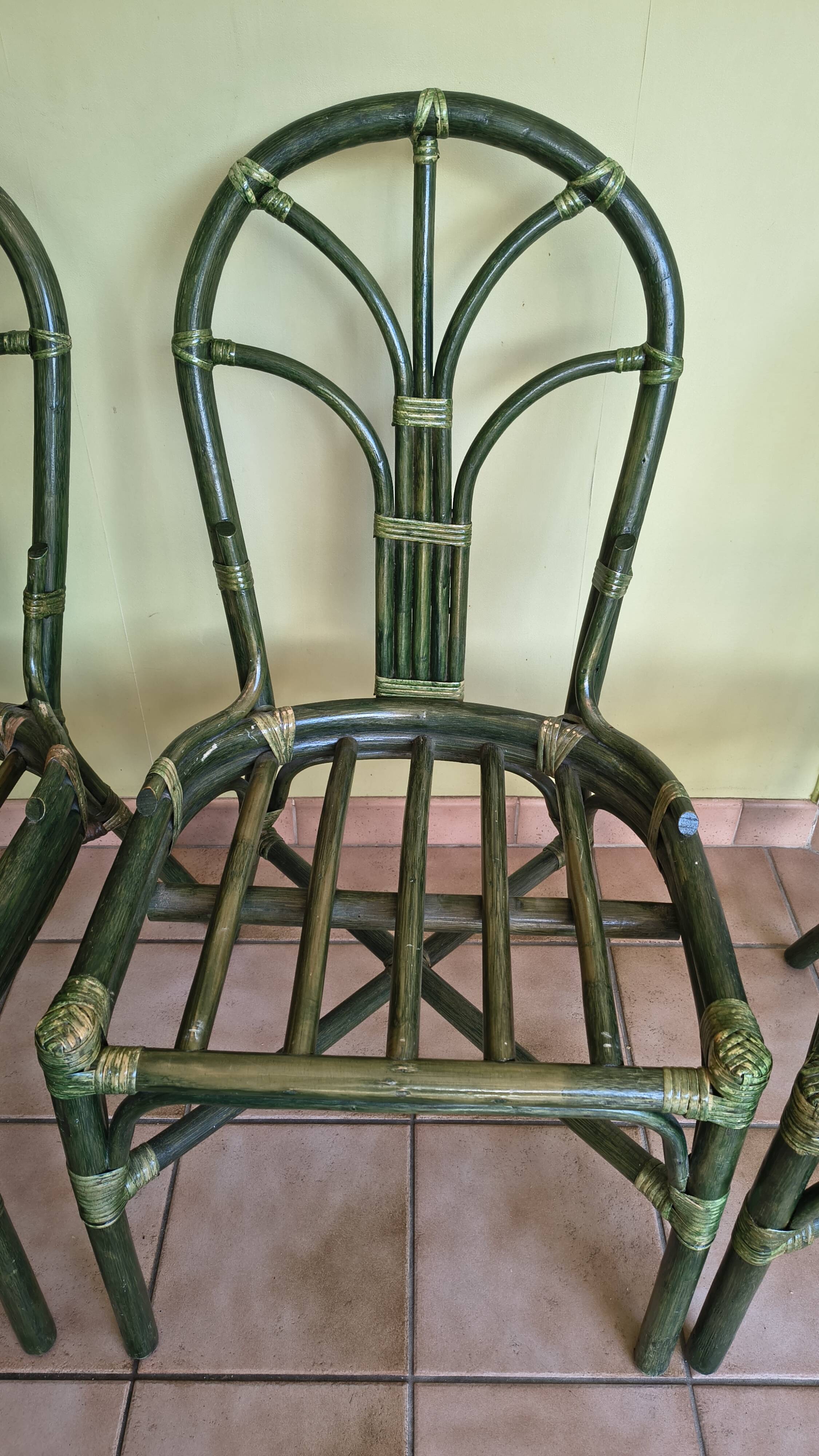 Round rattan table with glass top and 4 green rattan chairs.