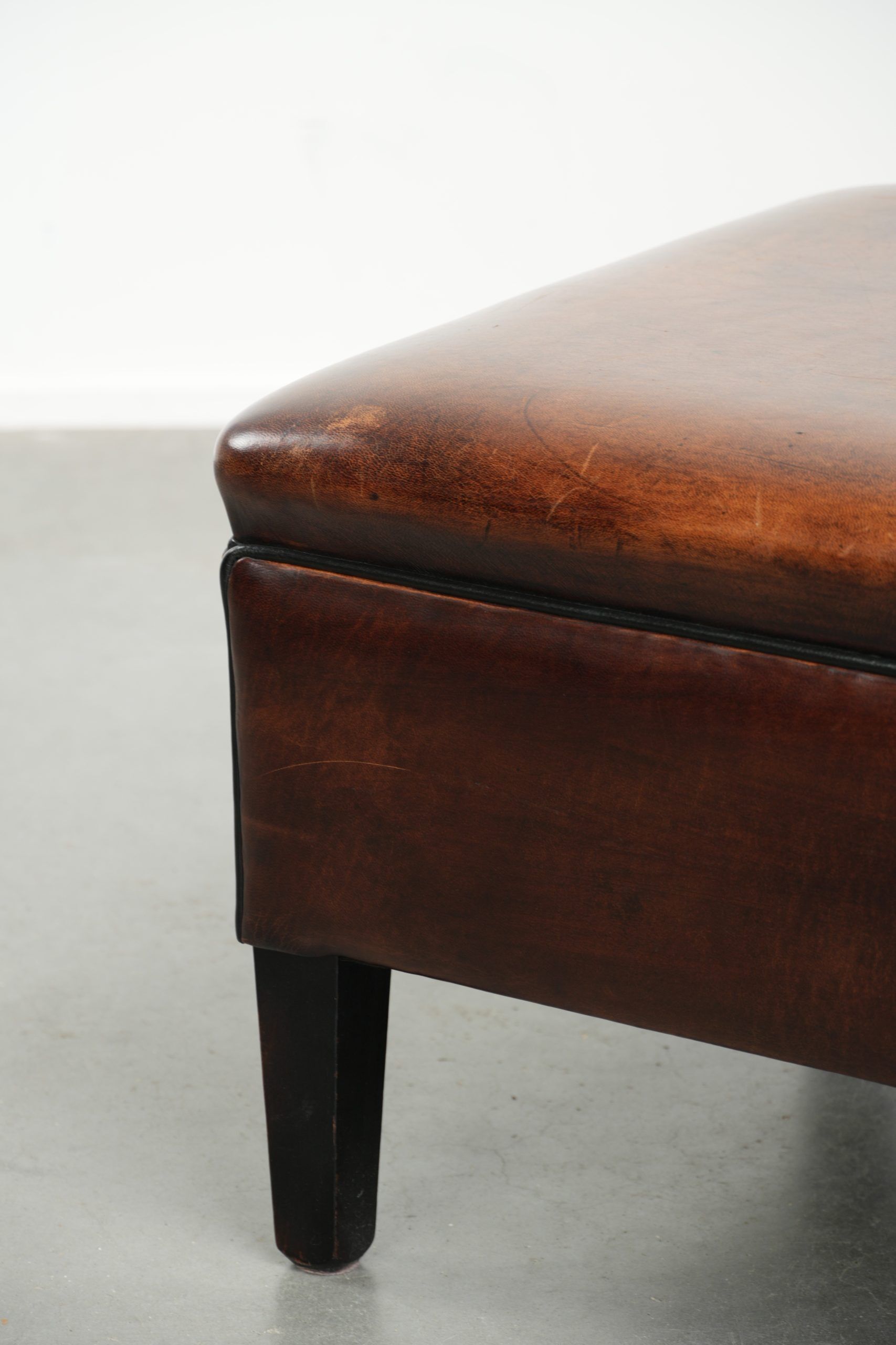 Large dark brown square ottoman made of sheepskin with black piping