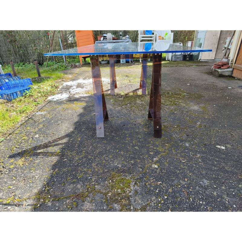 Vintage table with a glass top and smoked plastic trestle legs.