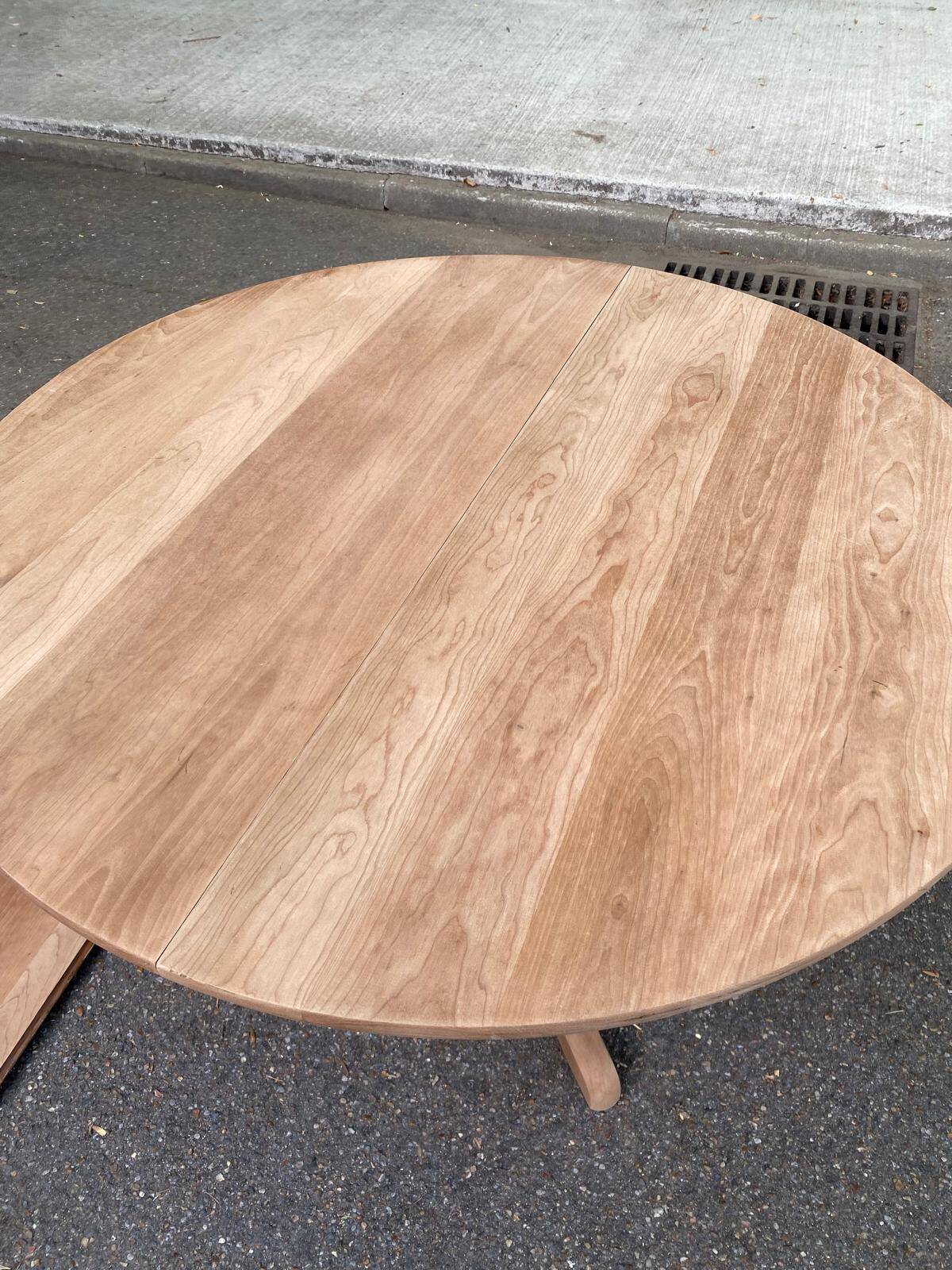 Large extendable round dining table stripped in solid cherry wood with a central leg.