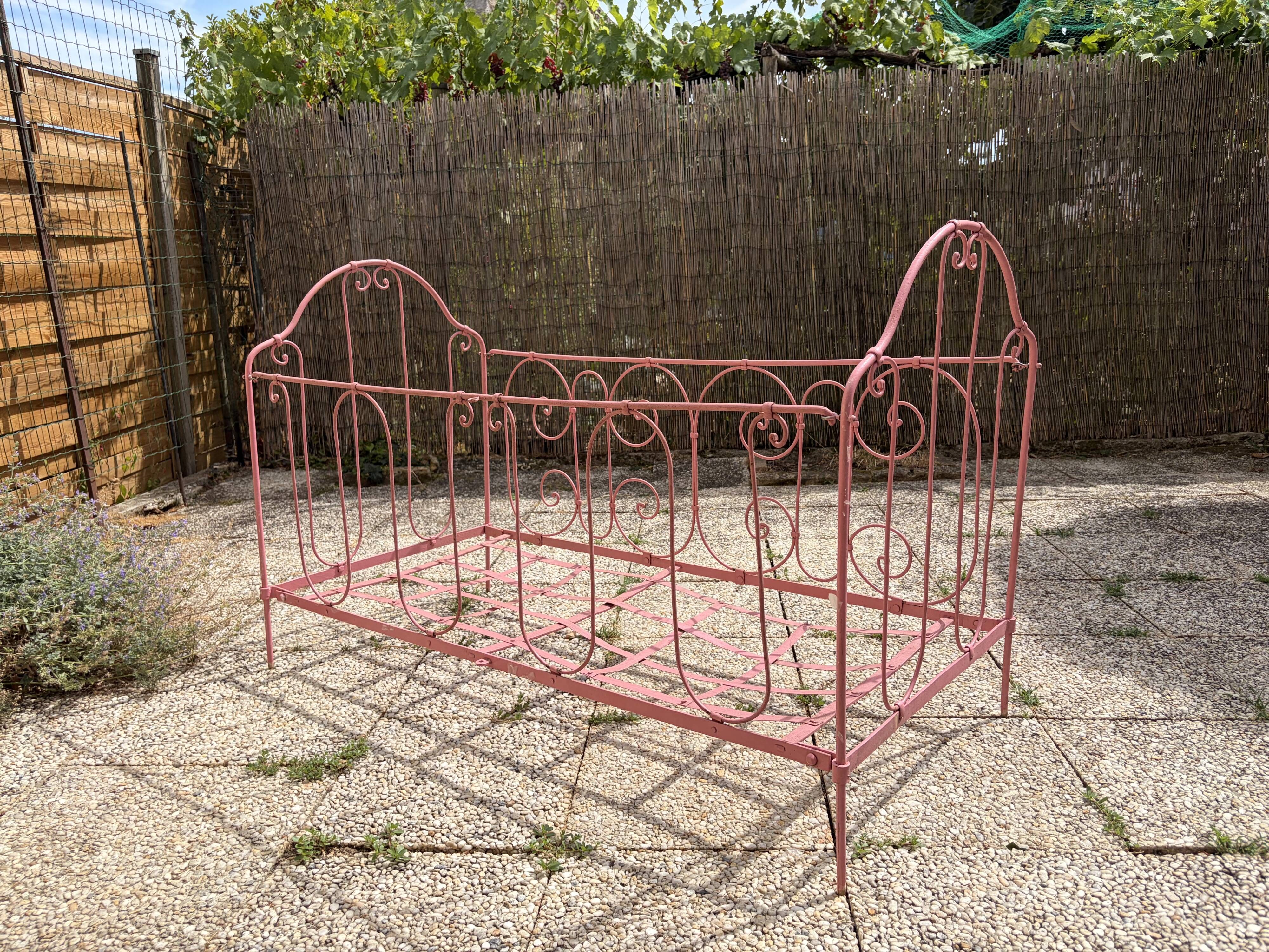 Old iron bed for children, painted pink with scrolls, romantic style.