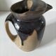 Stoneware jug with deep black drips on a sandy background.