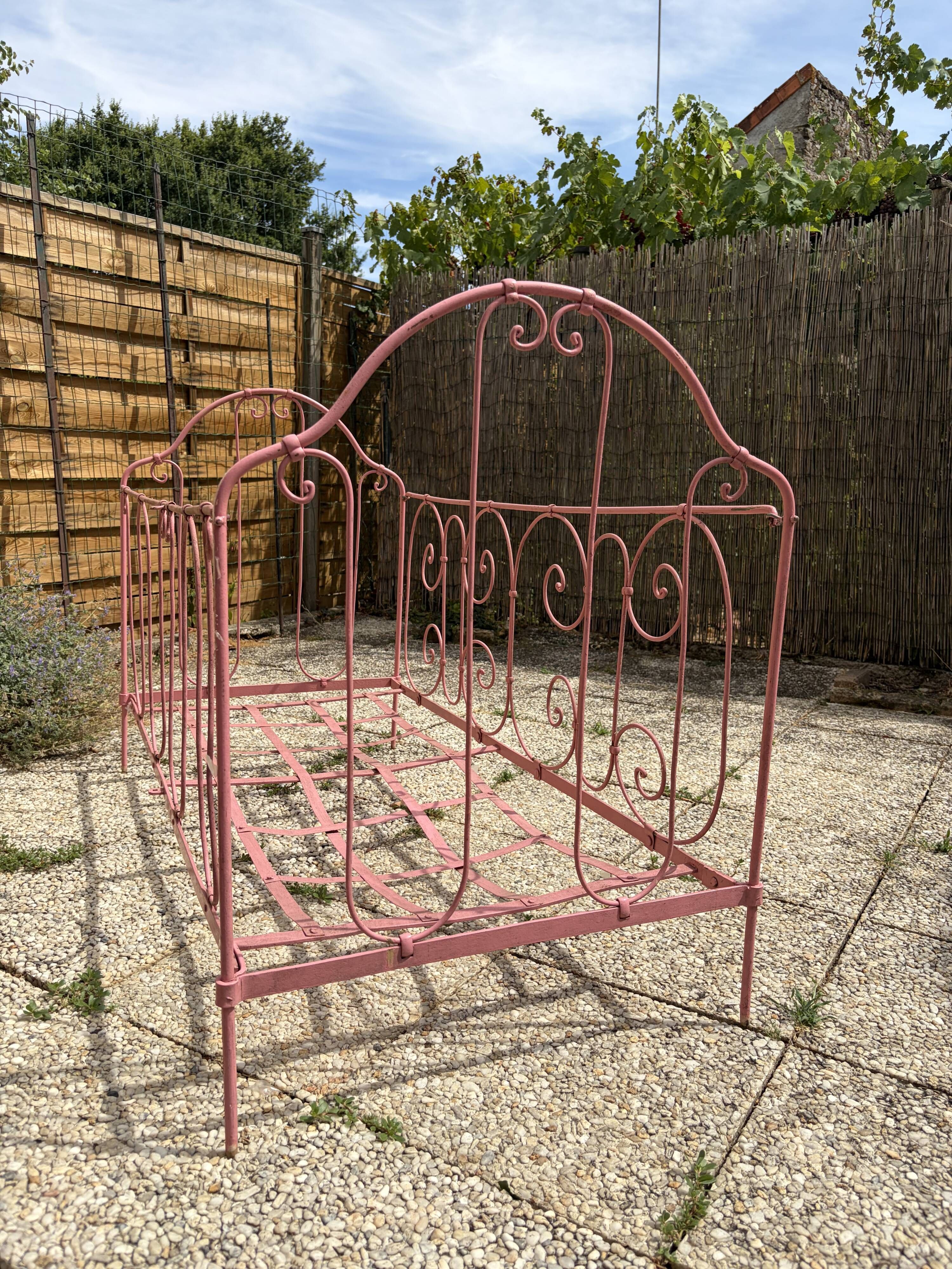 Old iron bed for children, painted pink with scrolls, romantic style.