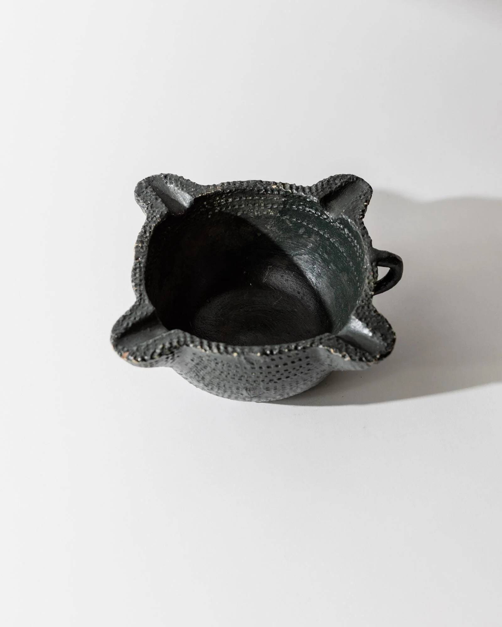 Vintage ceramic ashtray from the 1960s, black, hand-sculpted texture, organic shape.