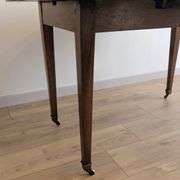 Antique wooden folding table with a patina and brass wheels.