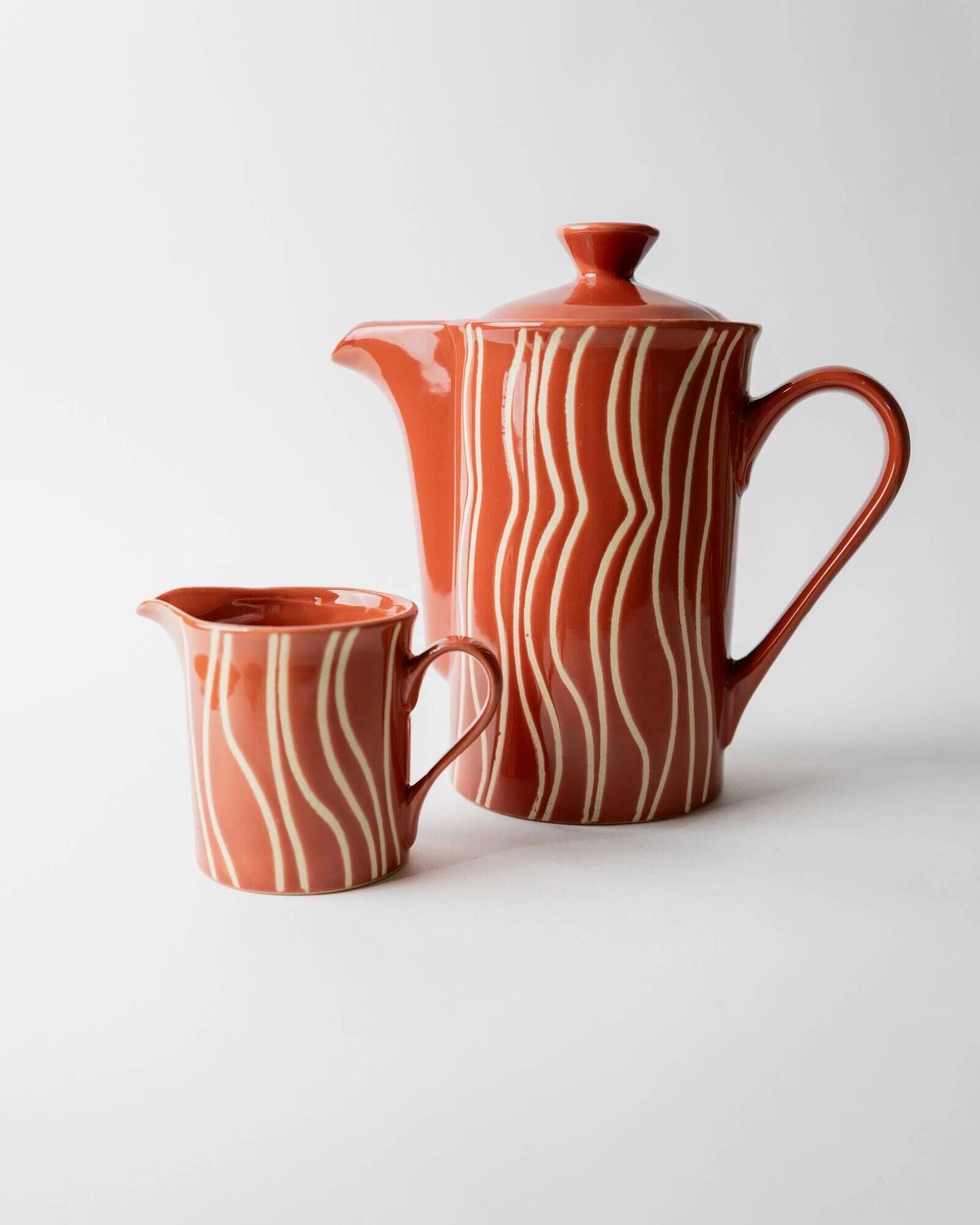 Vintage tea or coffee service in 1970s ceramic, teapot with lid and milk jug, rust orange with retro striped pattern, mid-century decoration, gift idea.