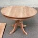 Large extendable round dining table stripped in solid cherry wood with a central leg.