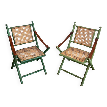 Paire de chaises safari pliantes façon faux-bambou patiné, dossiers et assises cannées et repose-bras en cuir