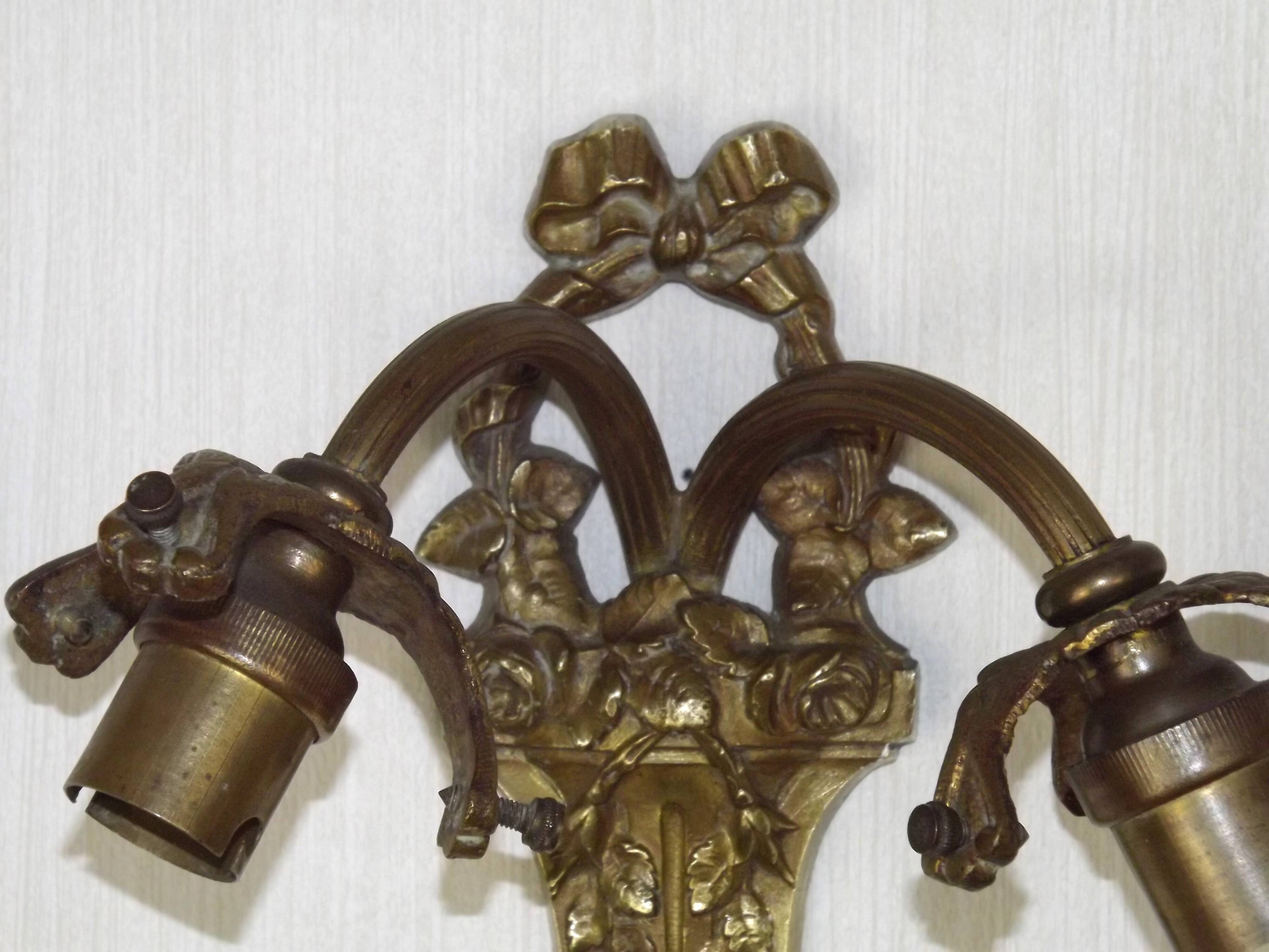 Double wall light in bronze in French Rococo style with white glass shades featuring patterns.