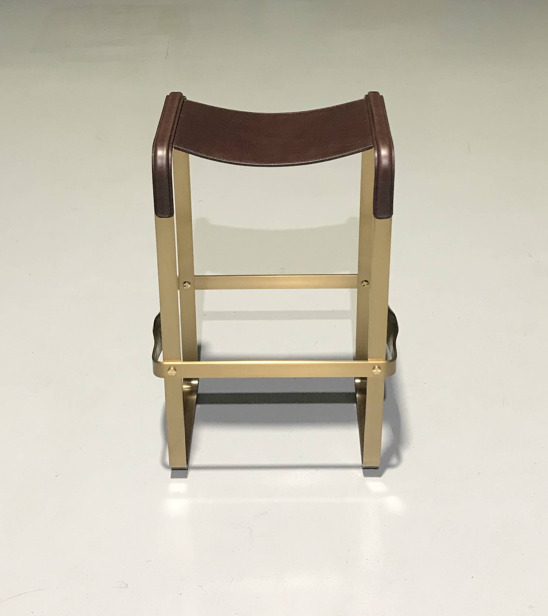 Bar stool in aged brass and brown leather.