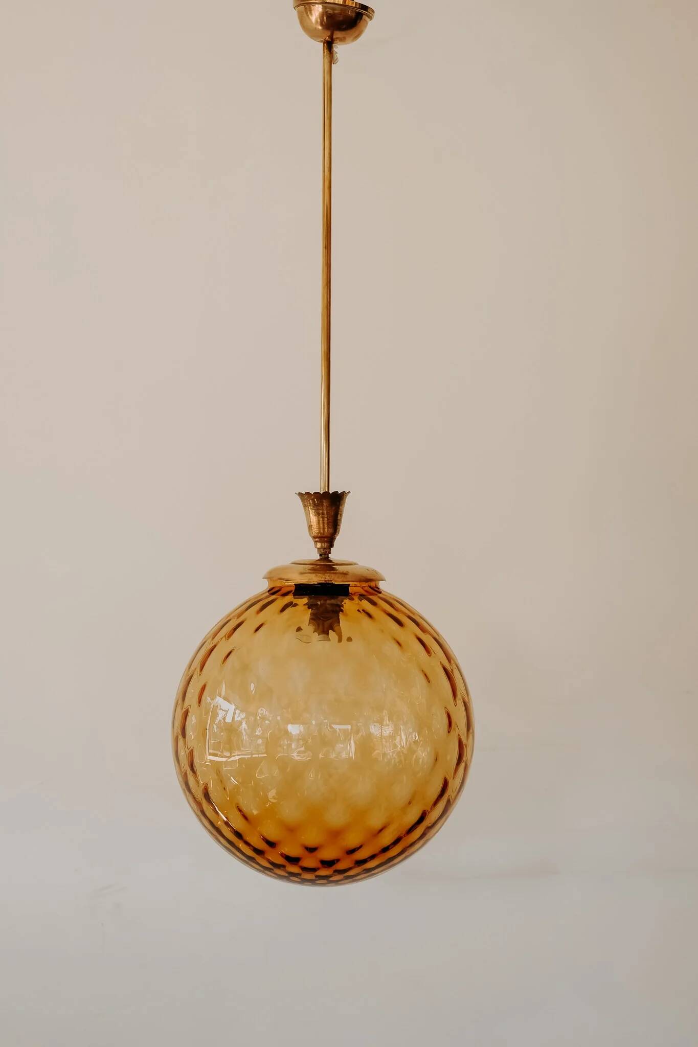 Brass pendant light with a round orange glass shade and a swirling structure.
