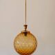 Brass pendant light with a round orange glass shade and a swirling structure.