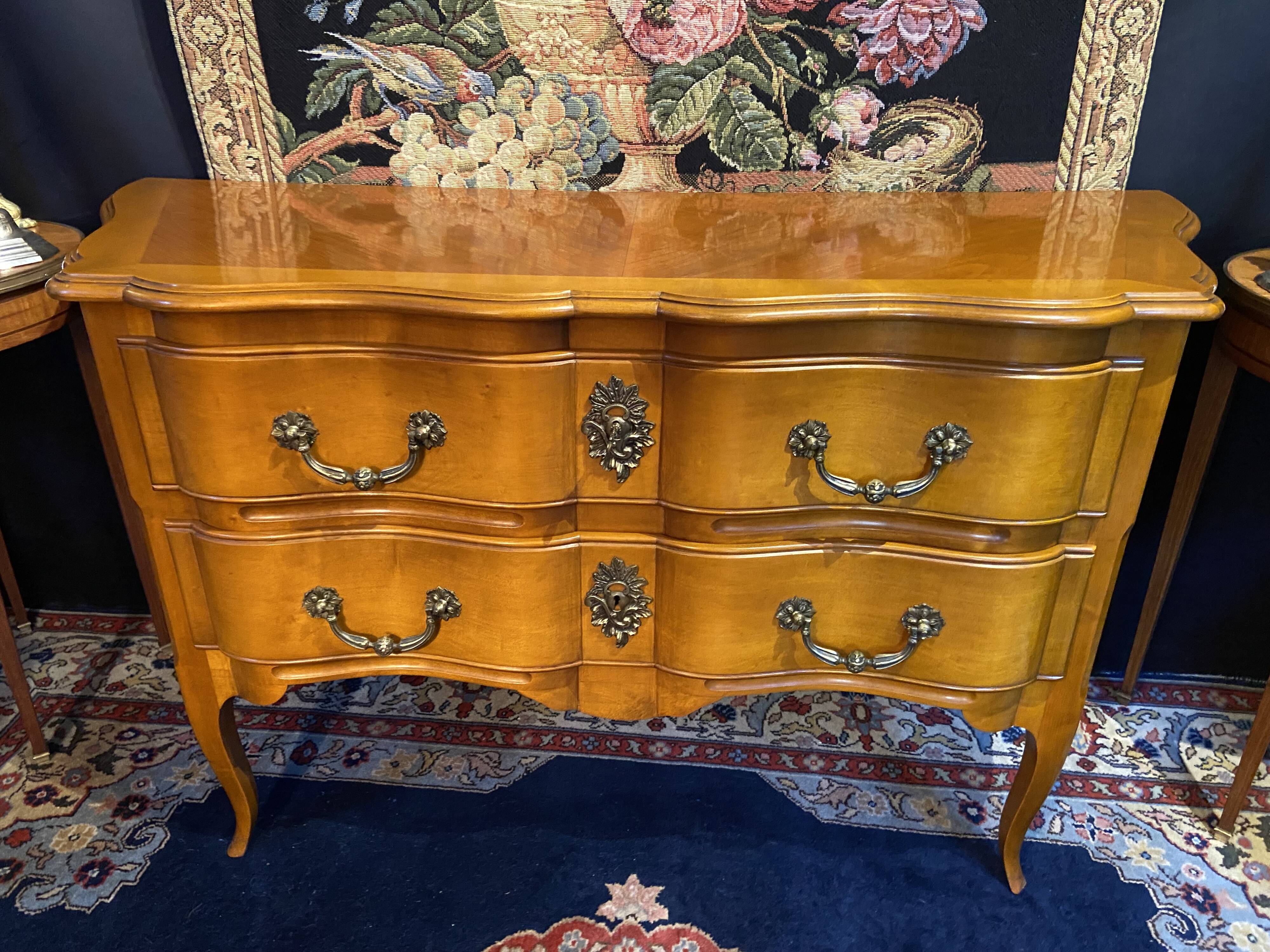 Large bow-fronted chest of drawers in blonde cherry with bronze ornamentation.