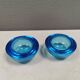 A set of iitalla candle holders in blue transparent glass.