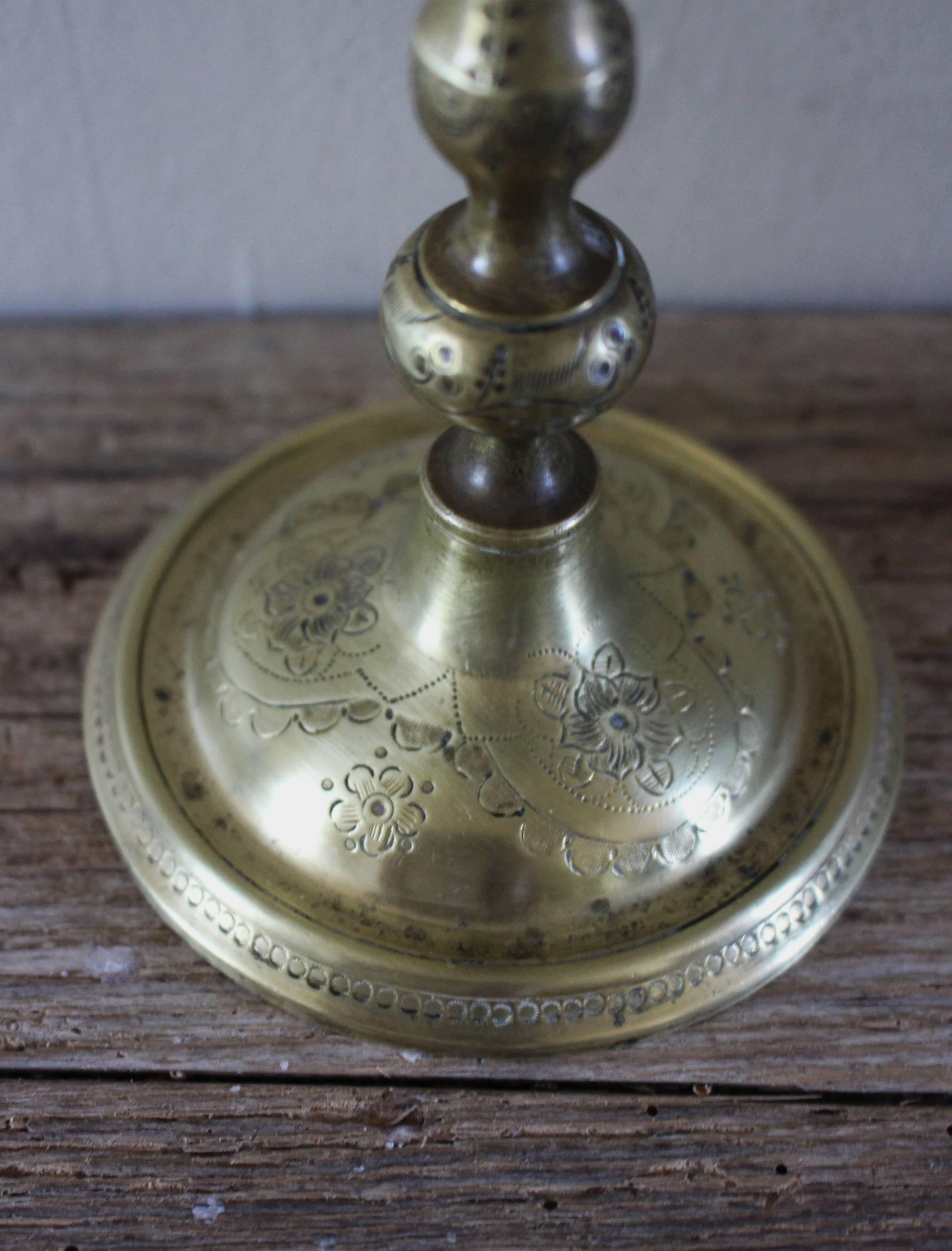 Brass candle holder with flowers and round shape.