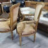 A pair of gilded wooden armchairs in the Louis XVI style.