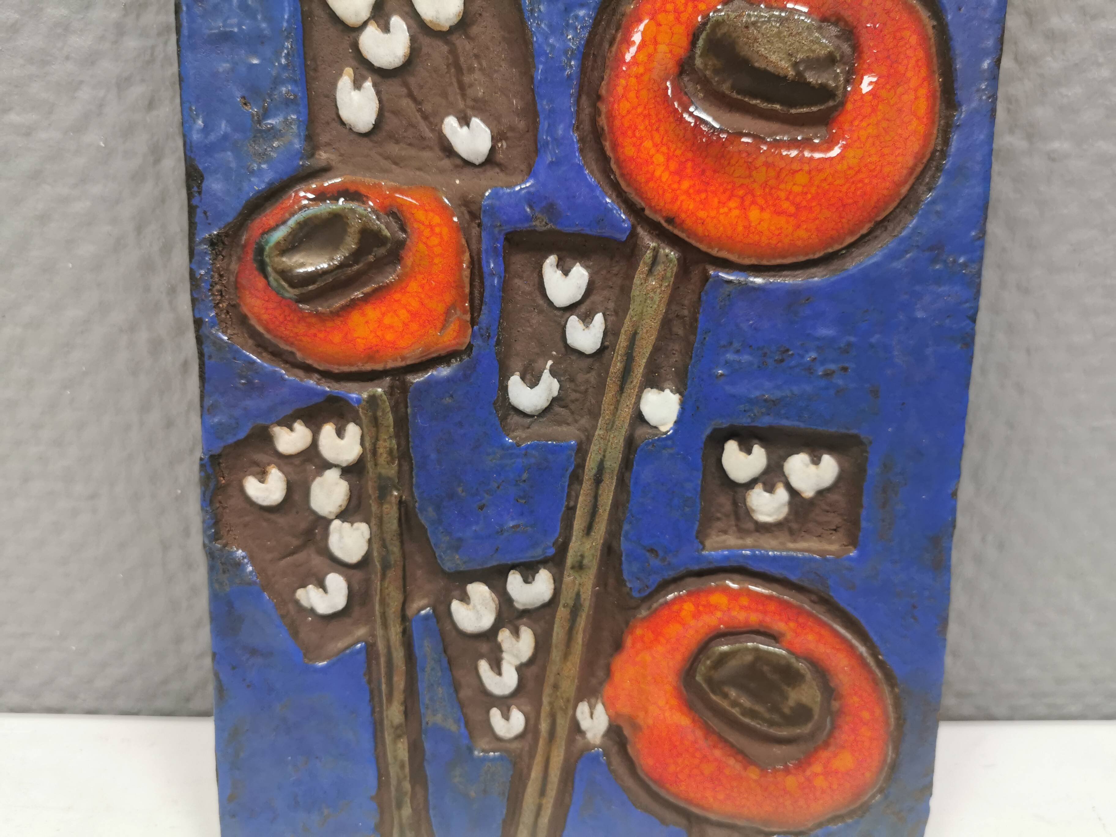 Ceramic relief in attractive blue with a motif of white/red flowers.