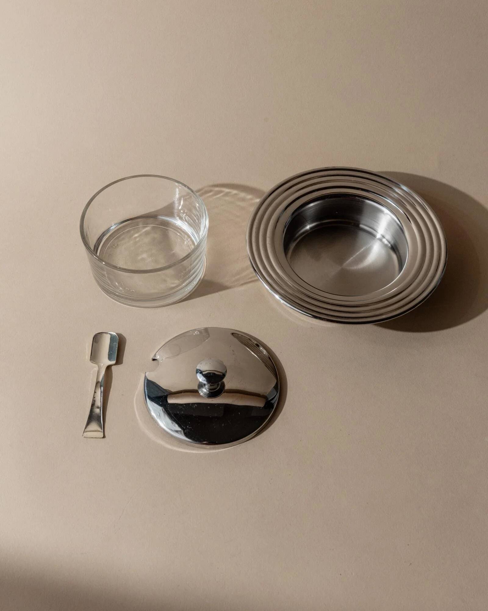 Vintage 1970s condiment pot made of glass and stainless steel with a lid, complete with a matching spoon.