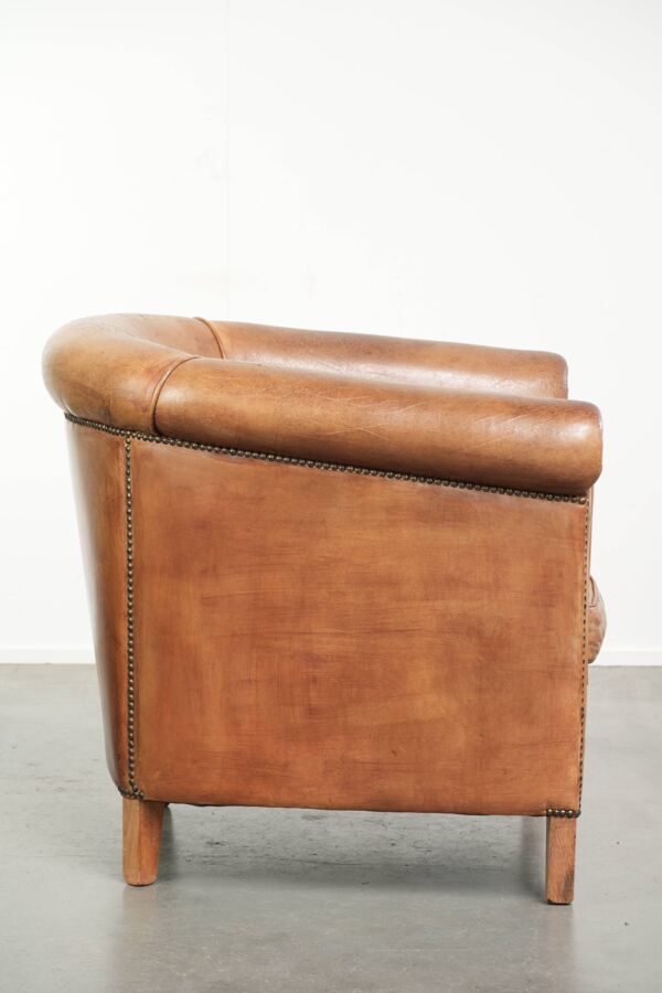 Fauteuil club en peau de mouton de couleur cognac, fini avec des clous décoratifs.