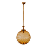 Brass pendant light with a round orange glass shade and a swirling structure.