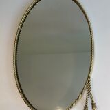 Oval brass mirror surrounded by a cord and adorned