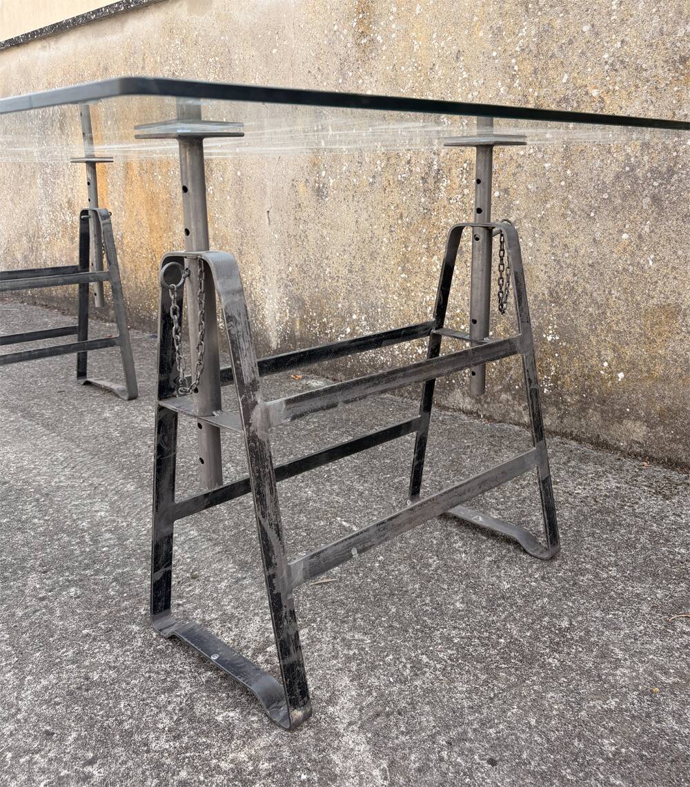 Large vintage industrial glass table with adjustable metal trestles.