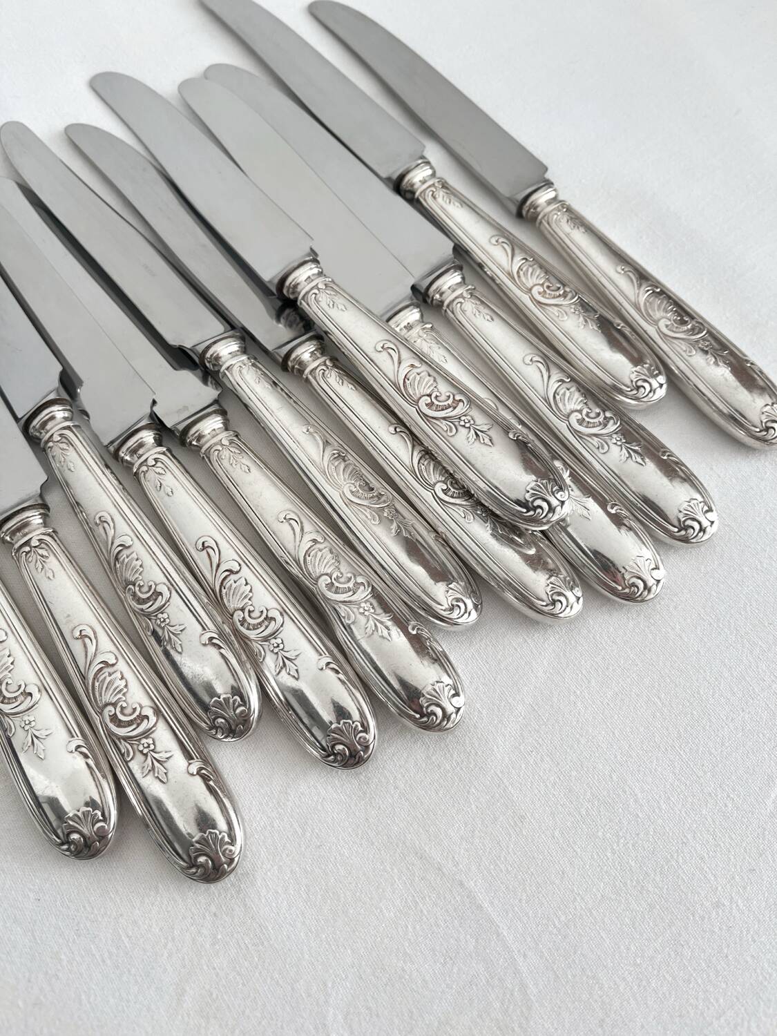 12 antique silver-plated knives with acanthus shell decoration and stainless steel blades.