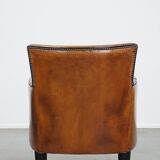 Cognac-colored sheepskin armchair with black piping and decorative nails