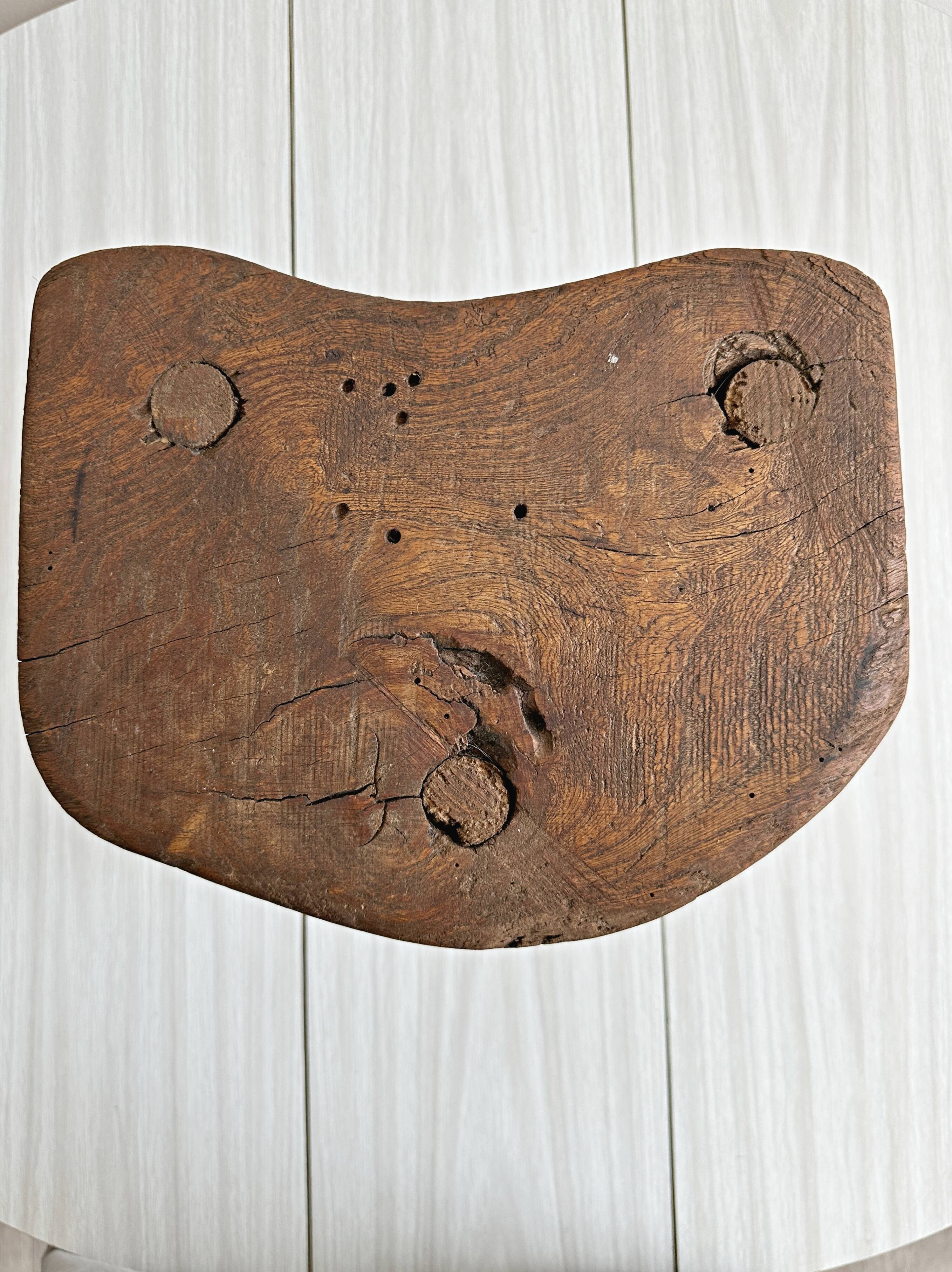 Antique three-legged stool made of raw solid wood.