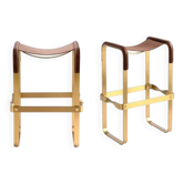 A pair of wanderlust stools without a backrest in brown with brass.