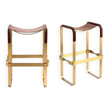 A pair of wanderlust stools without a backrest in brown with brass.