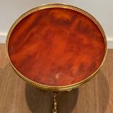 A round, neoclassical-style brass side table with a base decorated with dolphins and a red celluloid top encircled by an openwork gallery, attributed to the House of Jansen.