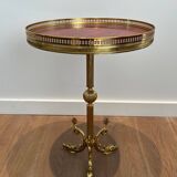 A round, neoclassical-style brass side table with a base decorated with dolphins and a red celluloid top encircled by an openwork gallery, attributed to the House of Jansen.