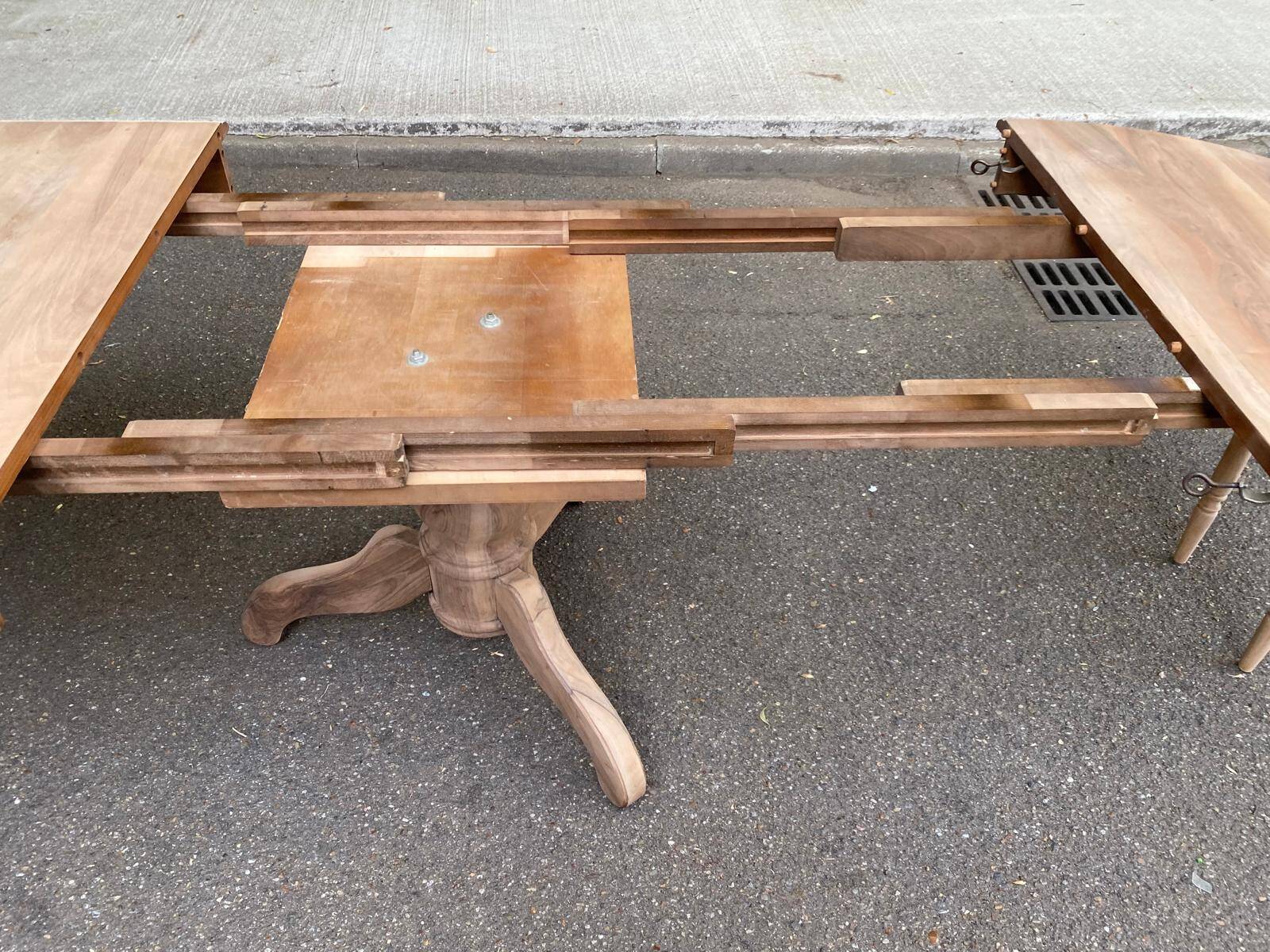Round extendable dining table stripped in solid raw walnut with a central leg.
