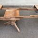 Round extendable dining table stripped in solid raw walnut with a central leg.