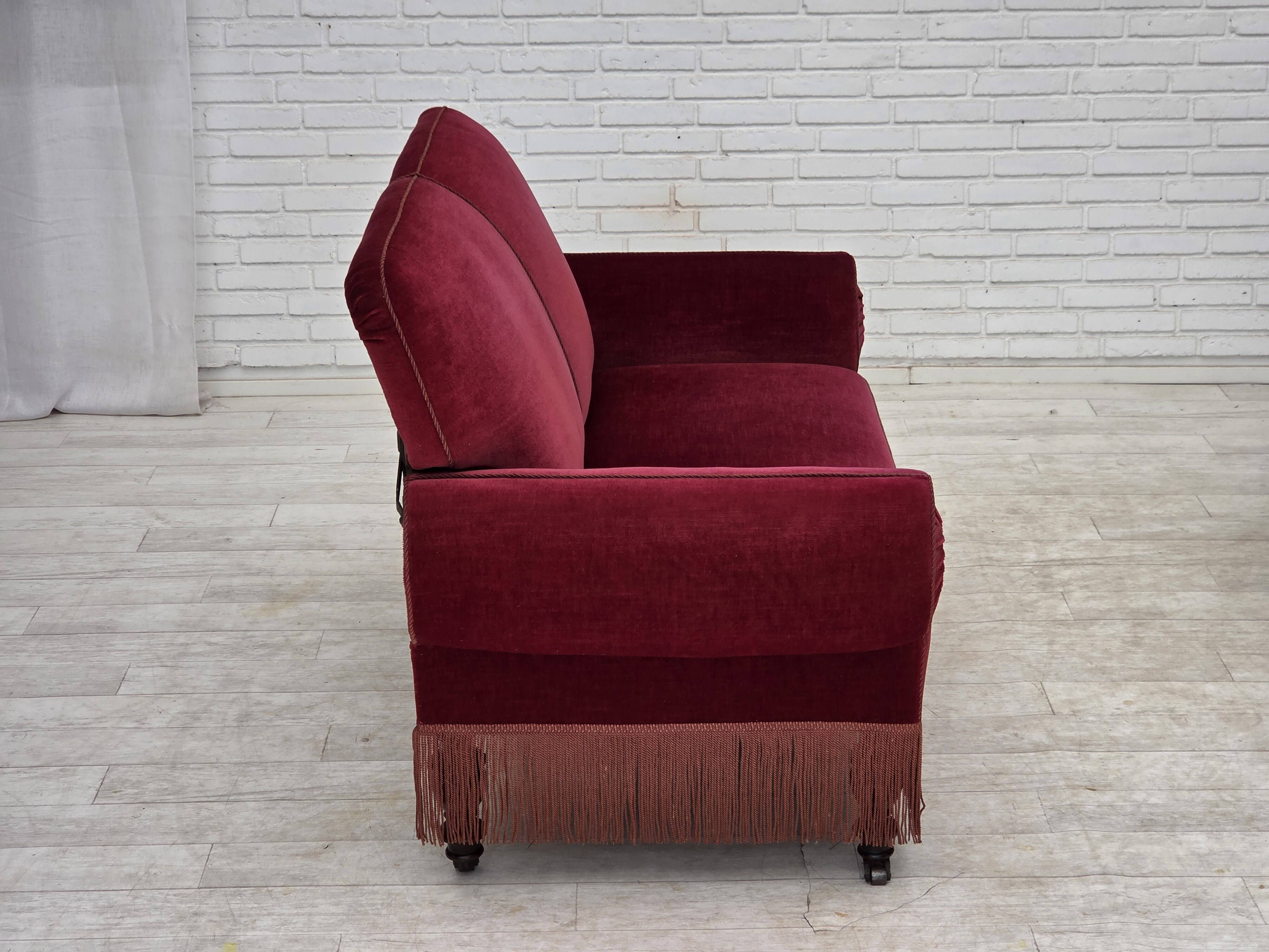 Canapé danois 2 places des années 1950, en velours rouge cerise avec accoudoirs rabattables.