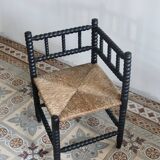 Antique black turned wood corner chair with a straw seat.