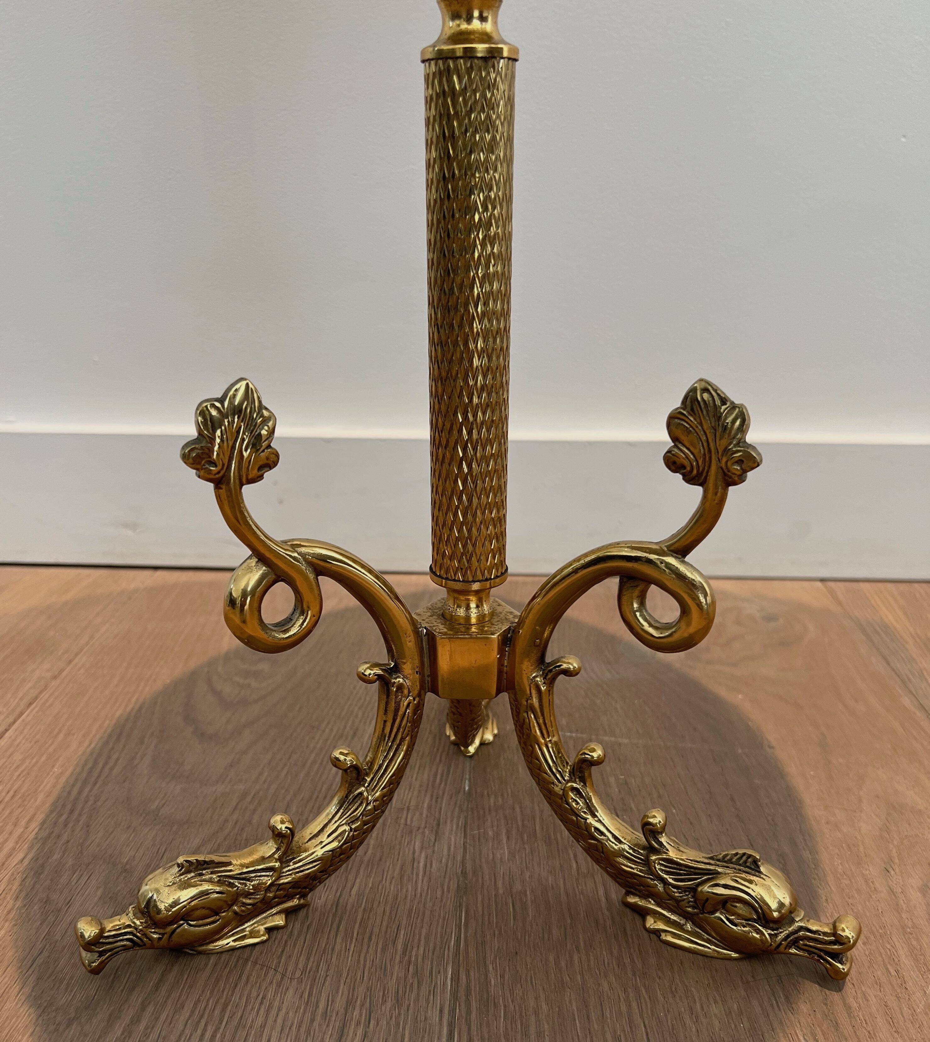 A round, neoclassical-style brass side table with a base decorated with dolphins and a red celluloid top encircled by an openwork gallery, attributed to the House of Jansen.
