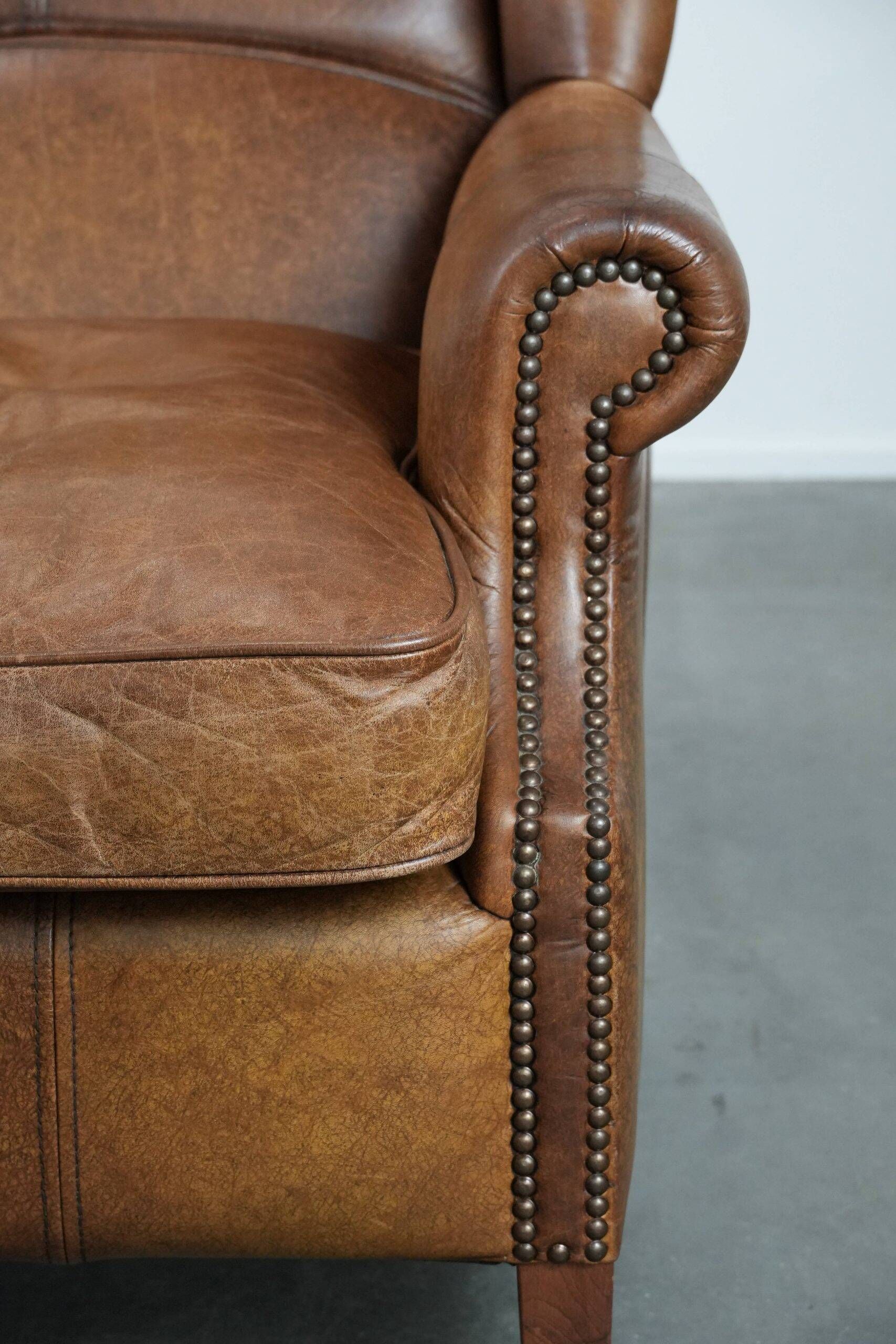 Fauteuil à oreilles de style anglais couleur cognac en cuir de vache.
