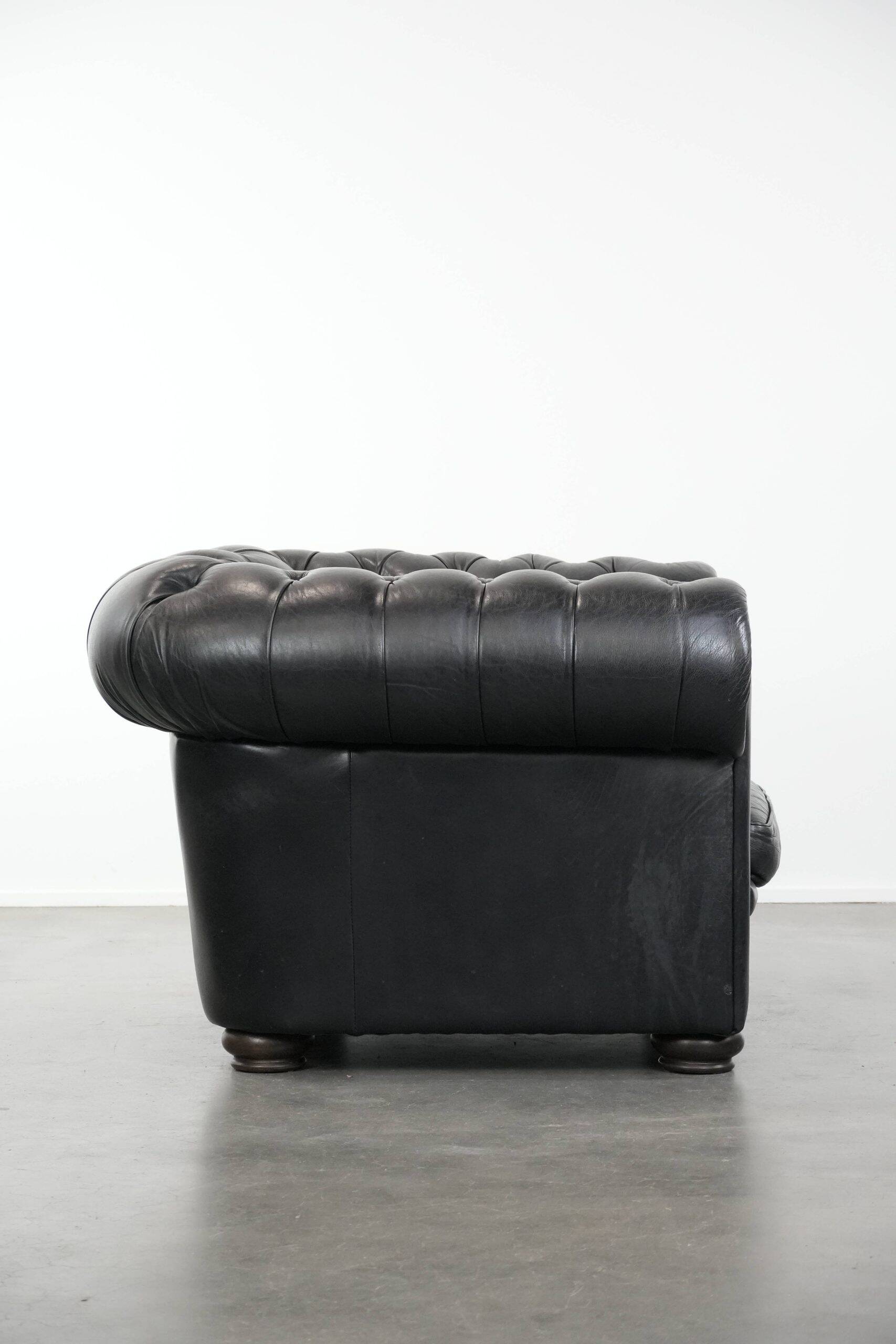 Ensemble composé d'un canapé chesterfield noir, d'un fauteuil et d'un pouf.