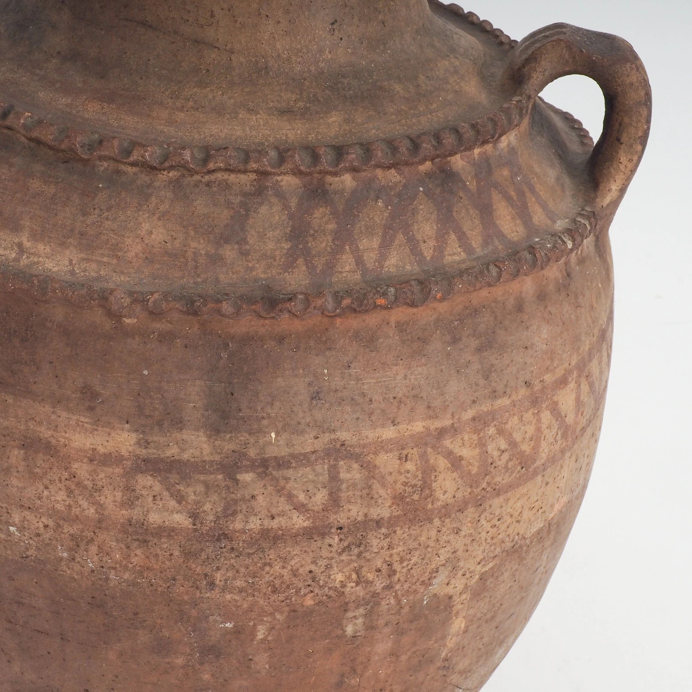 Vaisseau en terre cuite primitive avec des détails géométriques peints à la main.