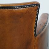 Cognac-colored sheepskin armchair with black piping and decorative nails