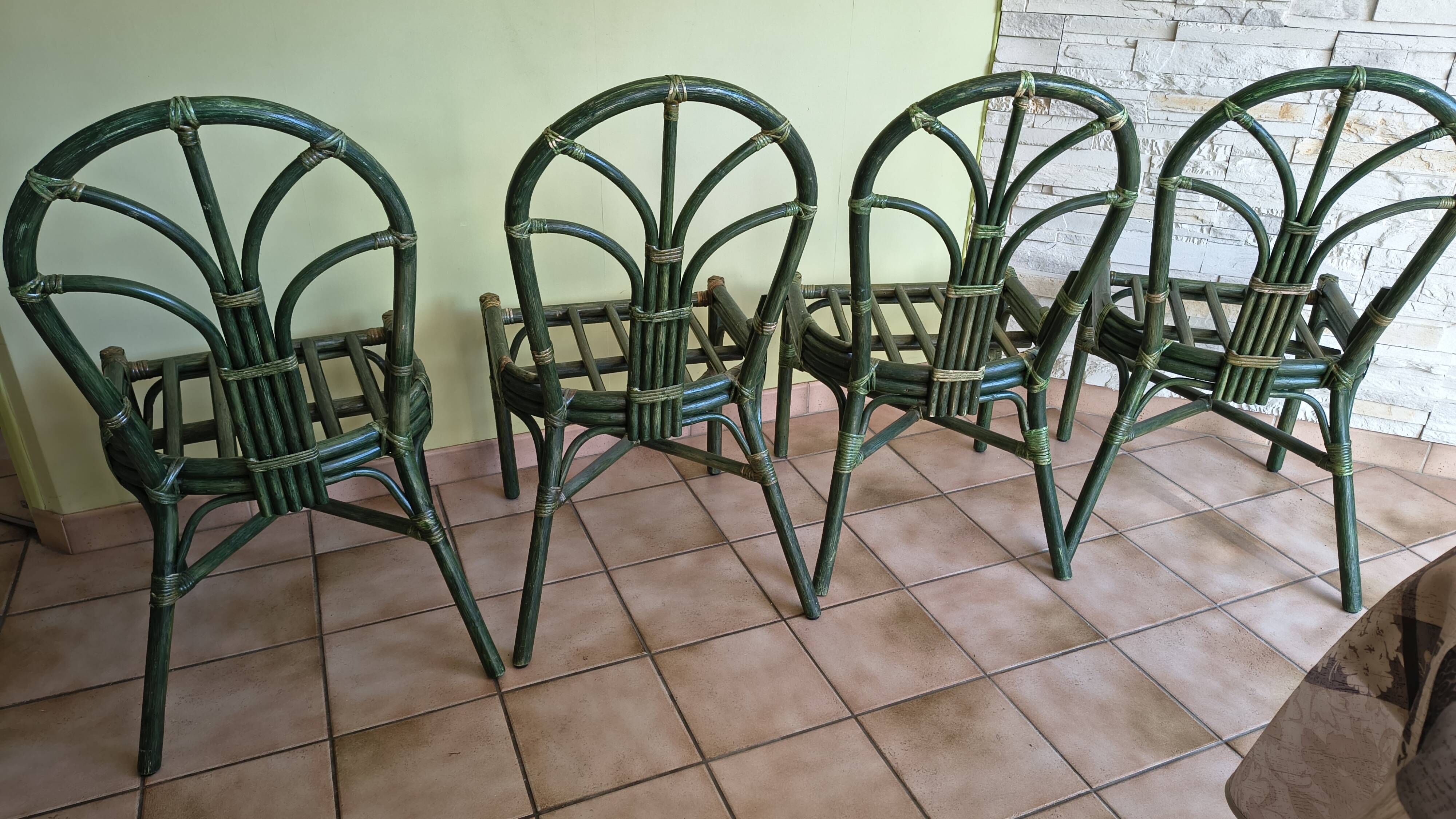 Round rattan table with glass top and 4 green rattan chairs.